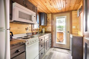 A compact kitchen with wooden walls, a microwave, stove, sink, and a refrigerator. - Blue Heron Treehouse - Private Hot Tub (Guild)