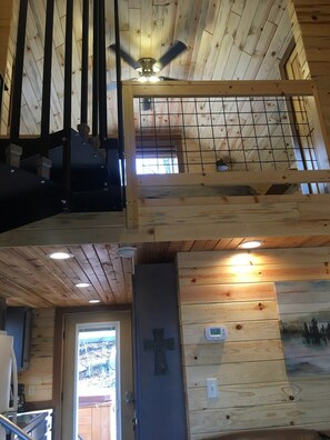 A wooden interior with a ceiling fan, a door with a cross, and a wall-mounted thermostat. - Blue Heron Treehouse - Private Hot Tub (Guild)