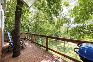 A wooden deck with a barbecue grill, chairs, and a tree.