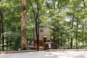 A rustic cabin with a wooden deck and a staircase leading to the entrance. - Blue Heron Treehouse - Private Hot Tub (Guild)
