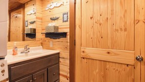 A wooden bathroom with a sink, mirror, and wooden cabinets. - Blue Heron Treehouse - Private Hot Tub (Guild)