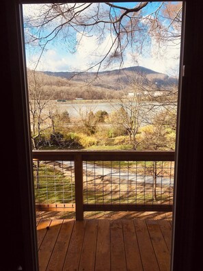 A wooden deck with a metal railing overlooking a landscape with trees, a body of water, and distant hills. - Blue Heron Treehouse - Private Hot Tub (Guild)