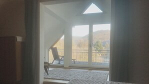Une chambre avec un grand lit, une chaise près d’une porte-fenêtre coulissante et une vue sur un balcon équipé d’une chaise et d’une table.