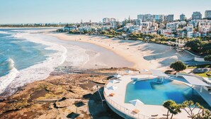 A coastal resort with a beachfront, a swimming pool, and a view of the city skyline. - Kings Beach Home Amongst Tranquil Gardens (Kings Beach)