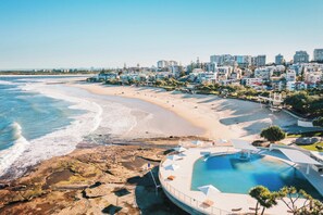 A coastal resort with a beachfront, a swimming pool, and a view of the city skyline. - Kings Beach Home Amongst Tranquil Gardens (Kings Beach)