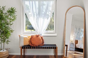 Una habitación con un banco, un espejo y una ventana con cortinas translúcidas.