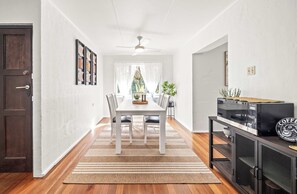 A modern kitchen with a dining area, wooden flooring, and a built-in TV. - Kings Beach Home Amongst Tranquil Gardens (Kings Beach)