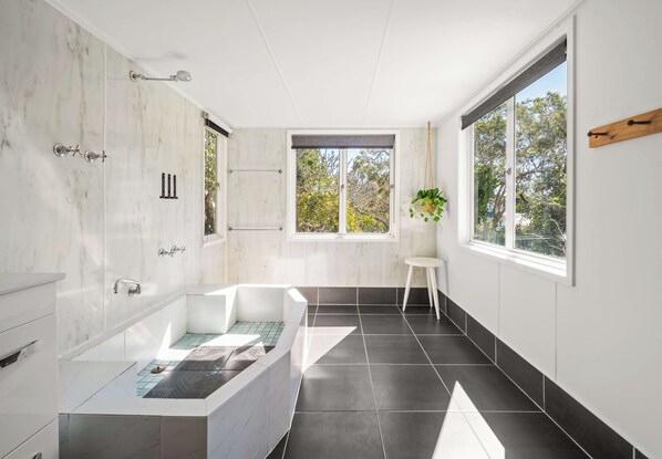 Un baño moderno con una bañera independiente, ducha y ventana con vistas a árboles.