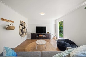 Un salon moderne avec un téléviseur à écran plat, un meuble de rangement en bois foncé, une table basse ronde et un fauteuil en forme de sac de haricots noir.