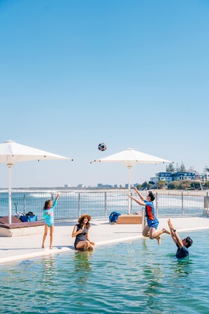 Zona de piscina con sombrillas, una red de voleibol y vista al mar.