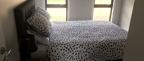 A bedroom with a bed, a nightstand, and a window.