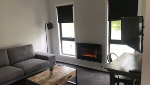 A modern living room with a grey sofa, a wooden coffee table, a TV mounted on the wall, and a fireplace. - Bright Racecourse View #2 (Bright)