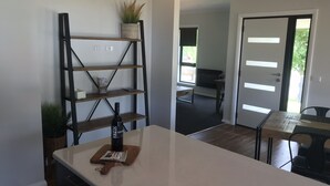 A modern kitchen with a central island, a wooden shelf with a plant, and a dining area with a table and chairs. - Bright Racecourse View #2 (Bright)