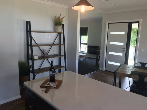 Une cuisine moderne avec un îlot central, une étagère en bois ornée d’une plante, et un coin repas comprenant une table et des chaises.