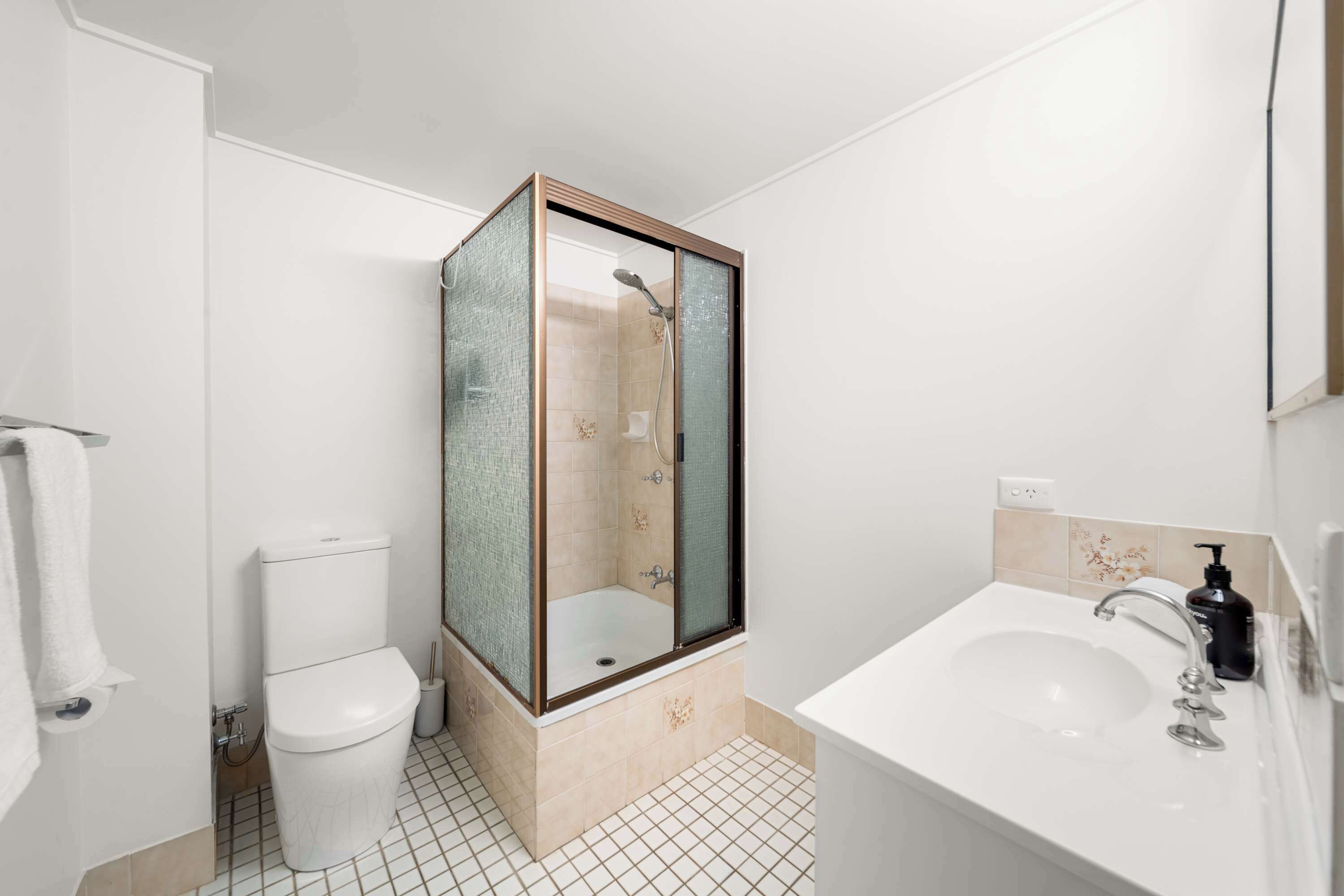 Un baño con ducha de vidrio, inodoro blanco y lavabo con espejo.