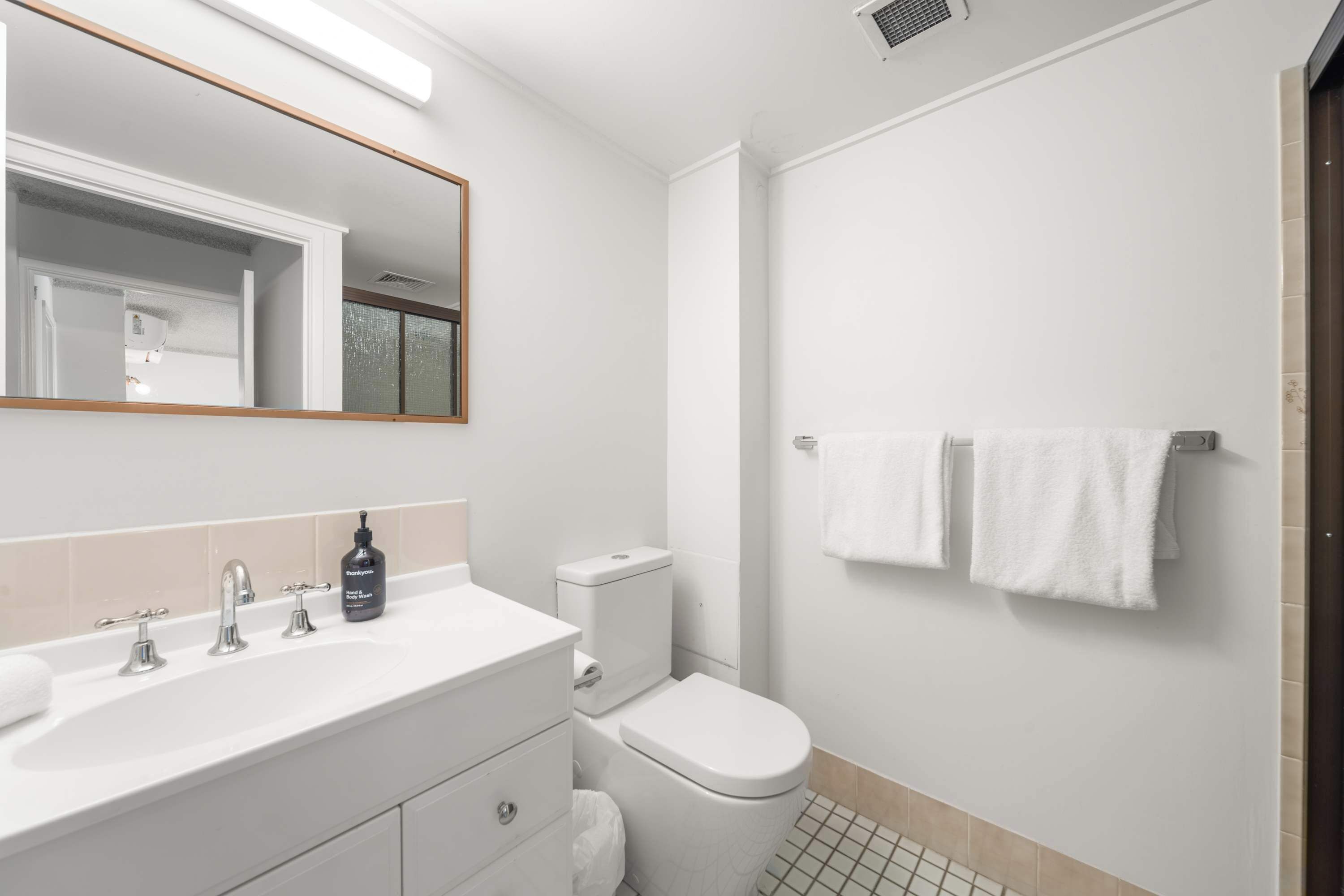 A modern bathroom with a white sink, three faucets, a toilet, and a mirror.