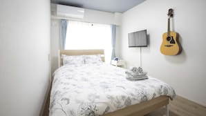 A bedroom with a bed, a guitar, a TV, and an air conditioner. - Koenji Street Apartment (Tokyo)