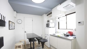 A compact kitchen with white cabinets, a black countertop, and a window above the sink. - Koenji Street Apartment (Tokyo)