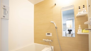 A modern bathroom with a bathtub, a shower with a handheld showerhead, a digital control panel, and a mirror. - Koenji Street Apartment (Tokyo)
