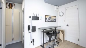 A compact kitchen with a refrigerator, a small dining table, and a clock on the wall. - Koenji Street Apartment (Tokyo)