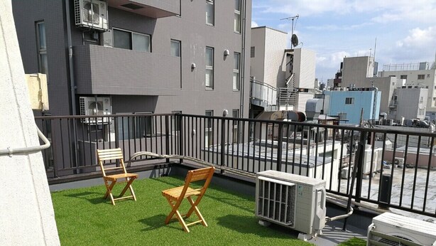 Una terraza en la azotea con césped artificial, dos sillas de madera y unidades de aire acondicionado.