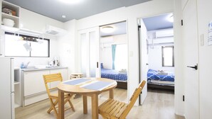 Una habitación compacta con kitchenette, un comedor con mesa y sillas, y una cama con colcha a rayas azul y blanca.