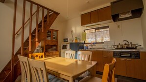 Uma cozinha com armários de madeira, uma mesa de jantar, cadeiras, micro-ondas, fogão e uma janela com cortinas.