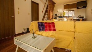 Uma sala de estar com um sofá amarelo, uma mesa de centro de vidro e uma escadaria de madeira.