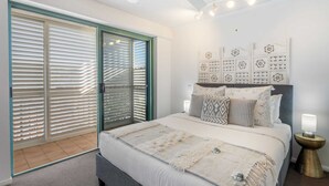 A bedroom with a large bed, a sliding glass door, a headboard with decorative panels, and a bedside lamp. - Oceanfront Views at Moffat Beach + Rooftop Terrace (Moffat Beach)
