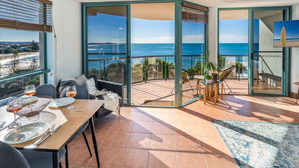 A balcony with a view of the sea, a dining table with plates and glasses, and a sofa. - Oceanfront Views at Moffat Beach + Rooftop Terrace (Moffat Beach)