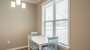 Ein Essbereich mit einem weißen Tisch und blauen Stühlen, einem Fenster mit Jalousien und einer Deckenleuchte.