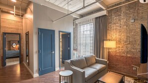A modern living room with a sofa, a small table, and a lamp. There is a brick wall and a wooden floor. - The Sessions Hotel, Bristol, a Tribute Portfolio Hotel (Bristol)