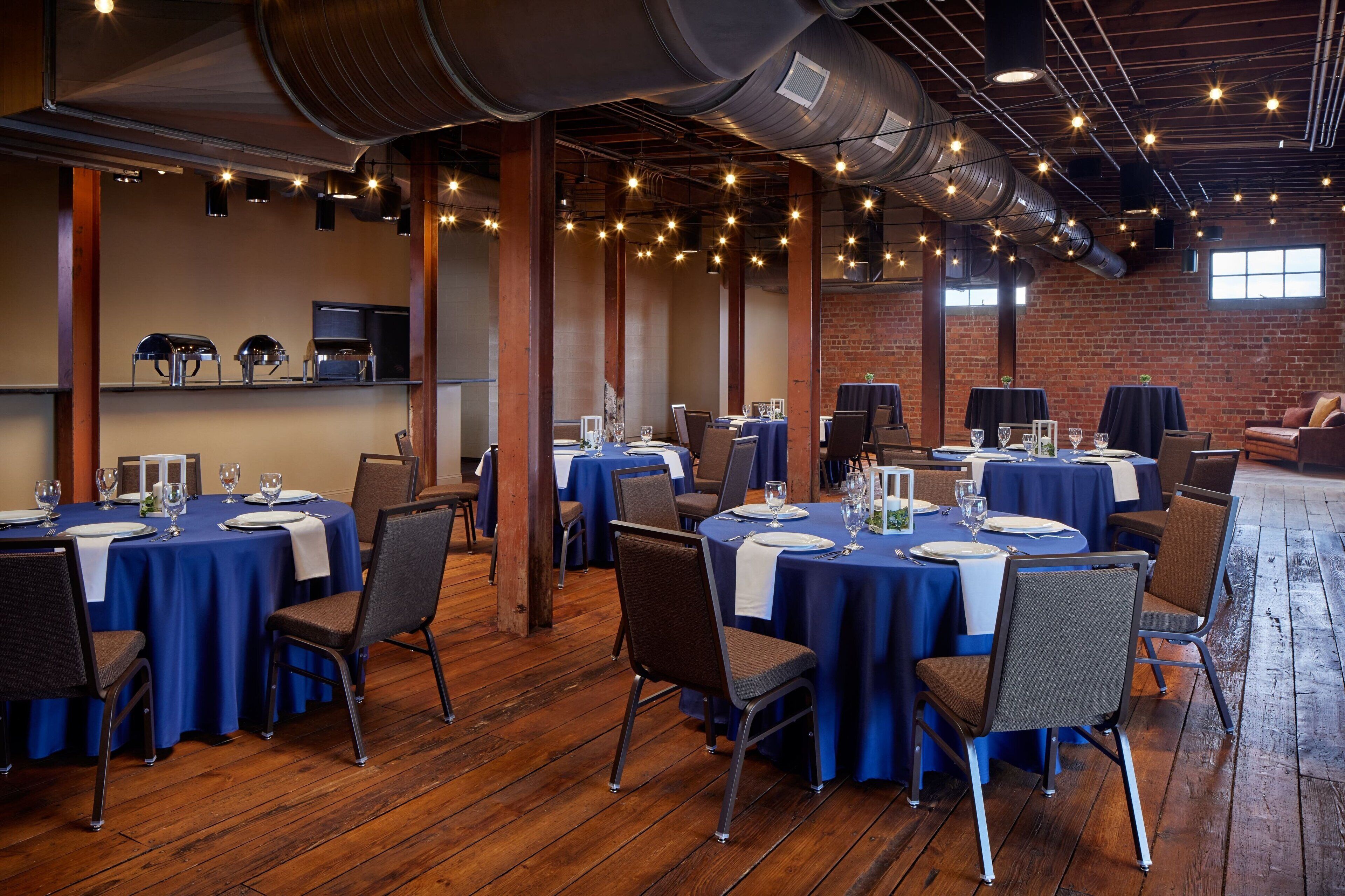 A restaurant with round tables covered in blue tablecloths, wooden floors, and brick walls.