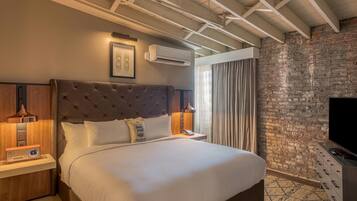 A hotel room with a large bed, a flat-screen TV, a brick wall, and a ceiling with exposed beams.