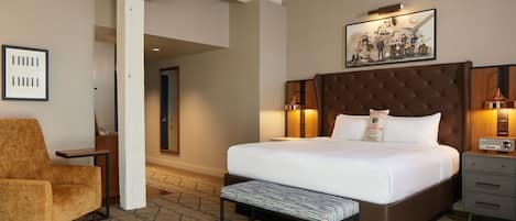 A hotel room with a large bed, a bench, a chair, a nightstand, and a wall-mounted TV.