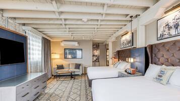 A hotel room with two beds, a TV, a sofa, and a dining area.