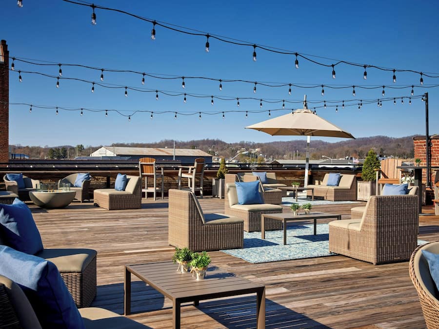 Una terraza al aire libre con mobiliario de mimbre, luces colgantes y un paraguas grande.