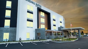 Un hotel moderno con un cartel grande que dice "SPRINGHILL SUITES BY MARATHON". Cuenta con una entrada destacada con una zona techada y un asta con la bandera estadounidense.