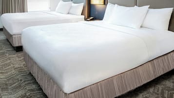 A hotel room with two beds, a carpeted floor, a nightstand with a lamp, and a window with curtains.