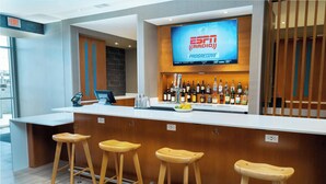 Zona de bar con taburetes, un televisor mostrando ESPN Radio y una variedad de botellas.