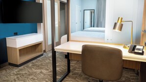 Una habitación de hotel con cama, escritorio, silla, televisión de pantalla plana y lámpara.