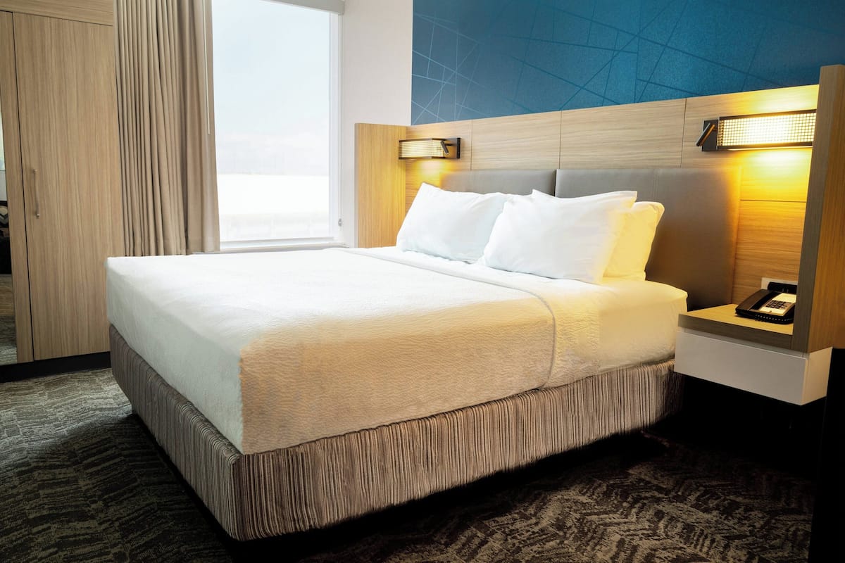 A hotel room with a large bed, a nightstand with a phone, and a view of the city.