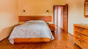 A bedroom with a wooden bed, a nightstand, a dresser, and a door leading to another room.