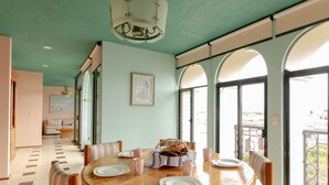 A dining area with a round wooden table, striped chairs, and large arched windows offering a view of the city.