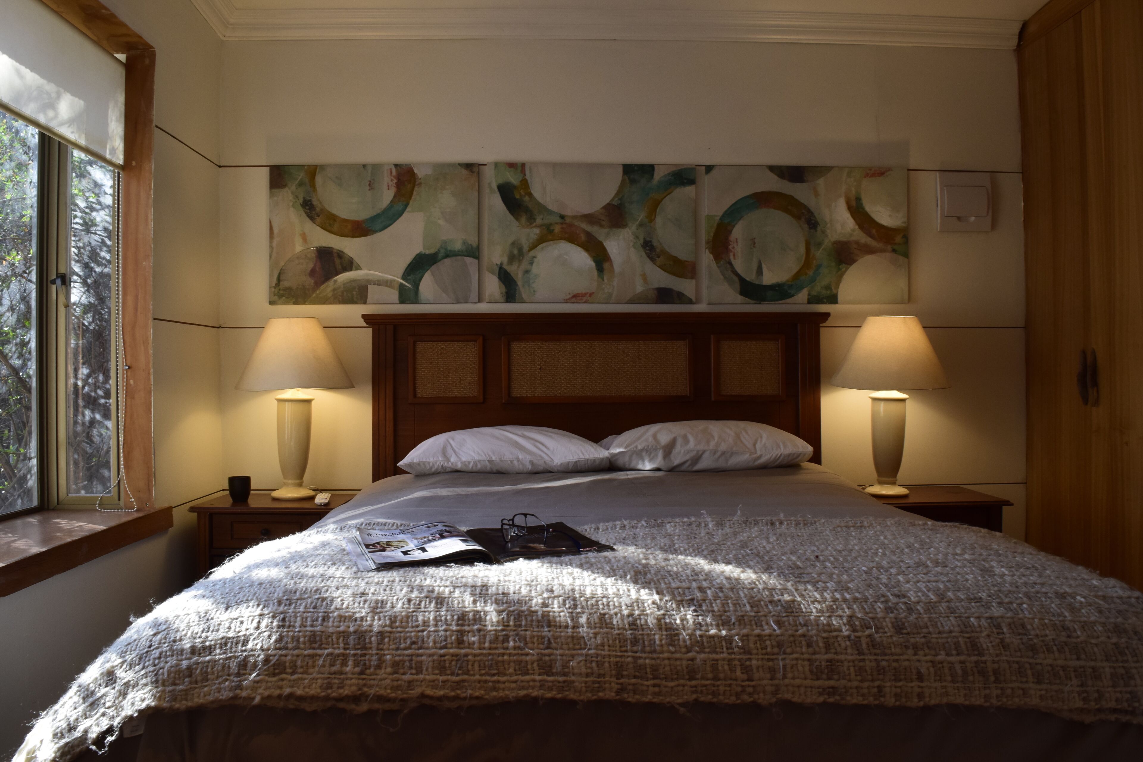 Un lit bien fait, recouvert d’une couverture à motifs, avec deux lampes de chevet et une fenêtre donnant sur les arbres.