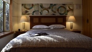 Un lit bien fait, recouvert d’une couverture à motifs, avec deux lampes de chevet et une fenêtre donnant sur les arbres.