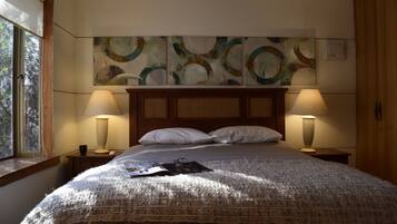 Un lit bien fait, recouvert d’une couverture à motifs, avec deux lampes de chevet et une fenêtre donnant sur les arbres.