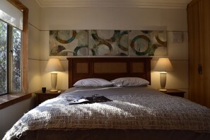 A neatly made bed with a textured blanket, two bedside lamps, and a window with a view of trees.