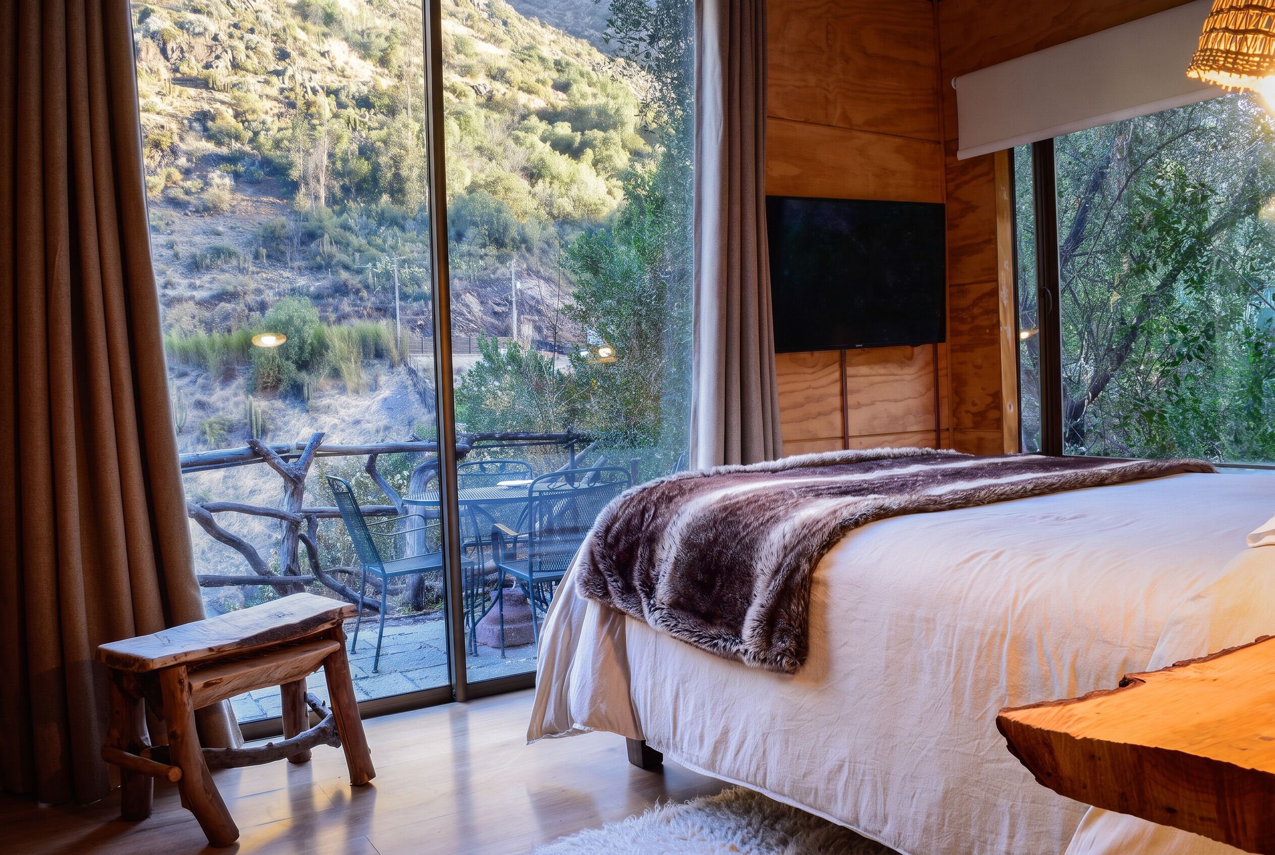 A bedroom with a large window, a bed, a wooden bench, and a television.