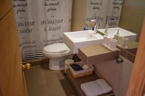 A bathroom with a toilet, sink, and a basket of toiletries.